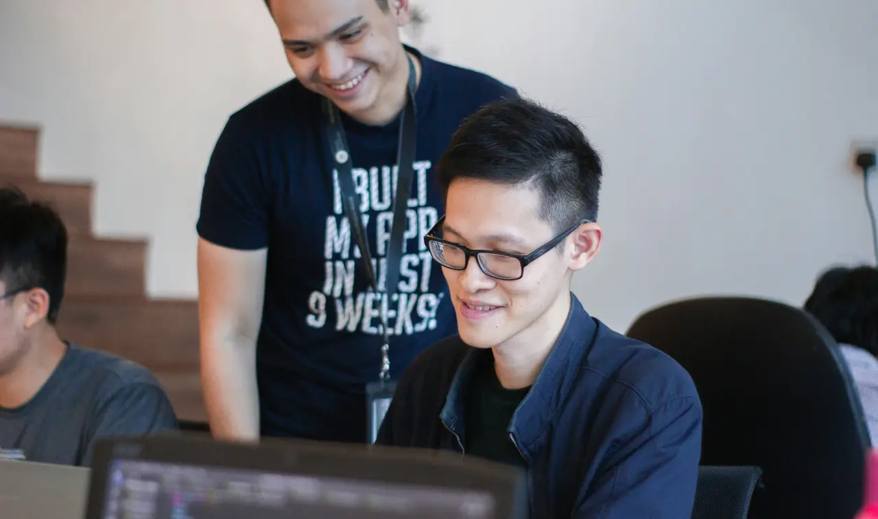 A developer leaning in to help a colleague at their screen